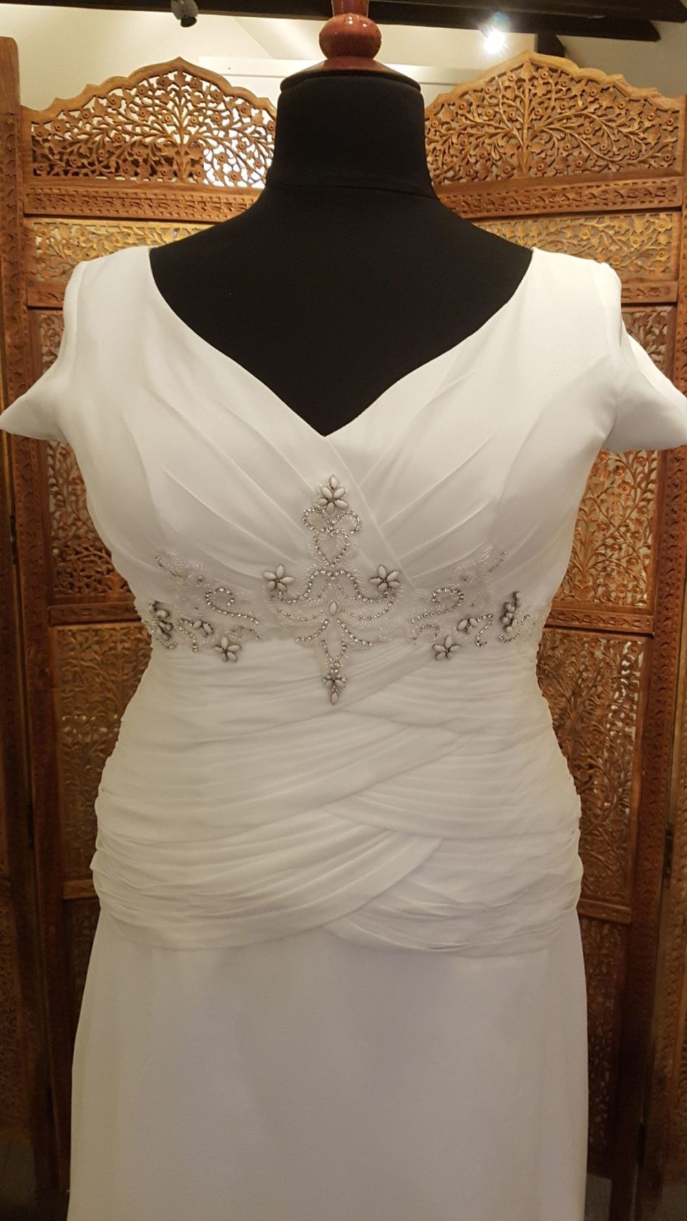 Smuk og enkel brudekjole i chiffon med en slank silhuet. Kjolen har draperinger omkring taljen, perlepynt under barmen og et lille ærme.