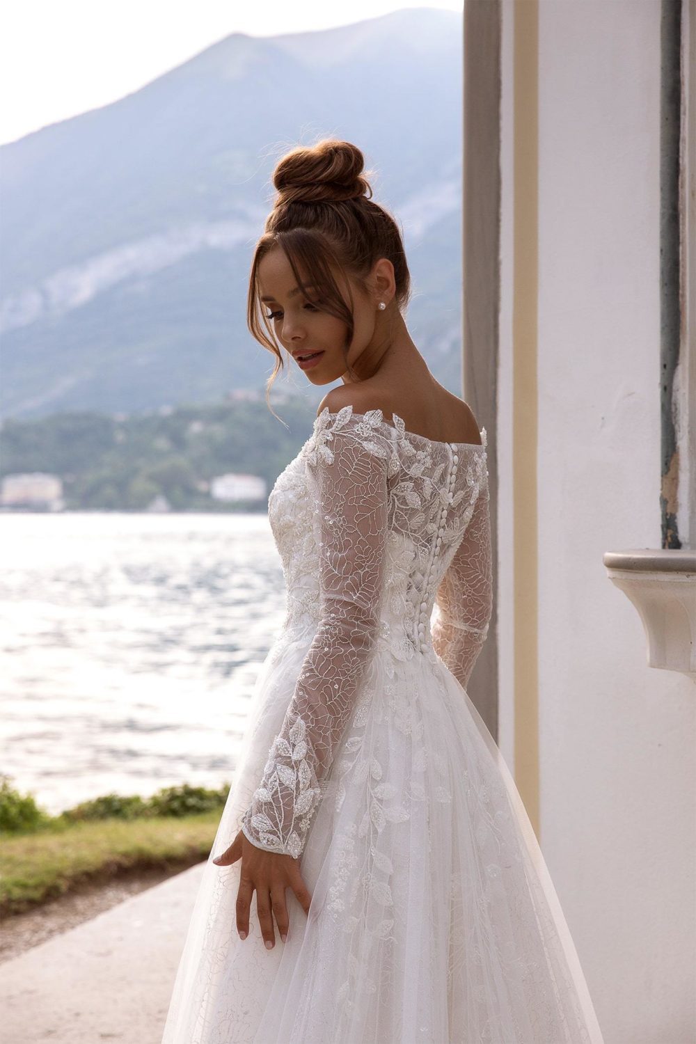 Maria Anette - Model 5016. A-line brudekjole med lange ærmer og bådudskæring. Kjolen har en blonde med sølvtråd og er desuden dekoreret med perlebroderi af blade og blomster.