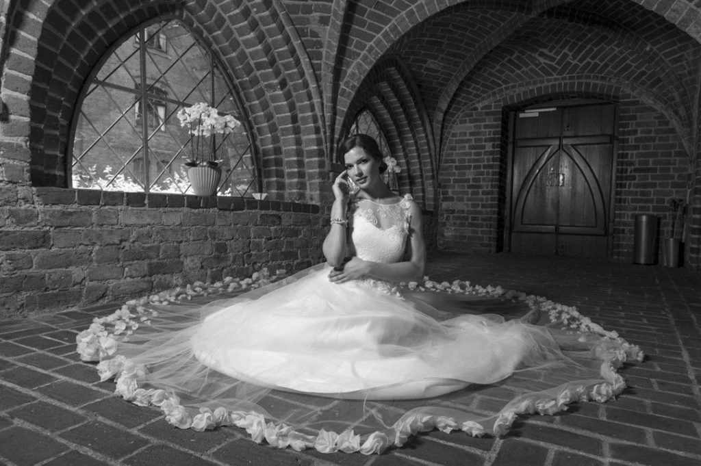 Smuk brud i brudekjole fra Budolfsen Kjoler. Hun sidder ned i et kirkerum. Sort-hvidt billede.