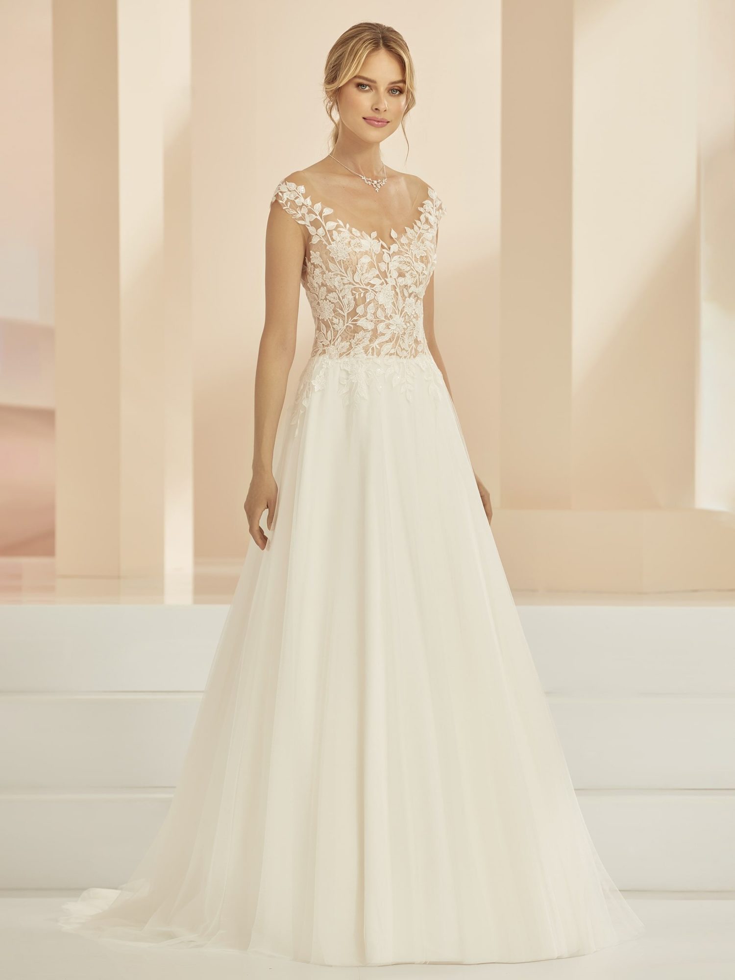 Bianco Evento model Heather. Smuk A-line brudekjole i tyl og dekorative blonder. Kjolen har off-sholder look og dyb udskæring på ryggen.