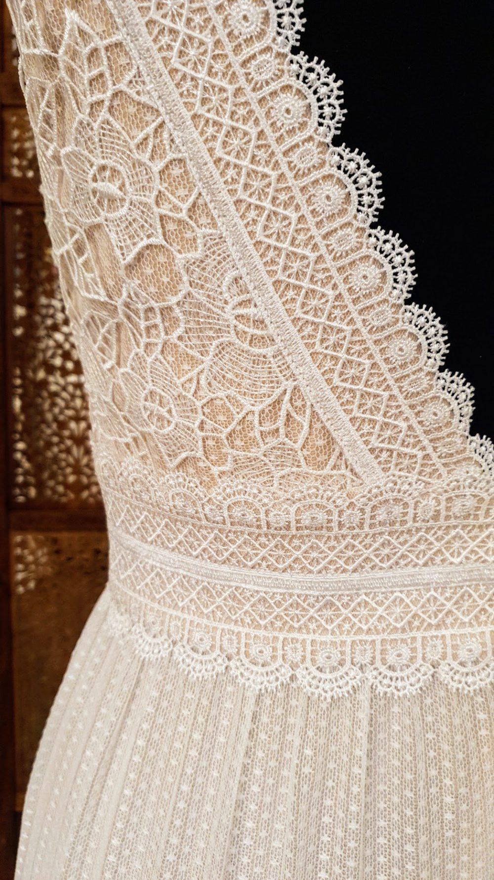 Virkelig smuk boho-brudekjole fra Milan, hvor de grafiske blonder træder så smukt frem på en champagnefarvet bund. Kjolen har v-udskæring foran og bagpå og brede stropper. Skørtet er i prikket tyl og har et lille slæb.
