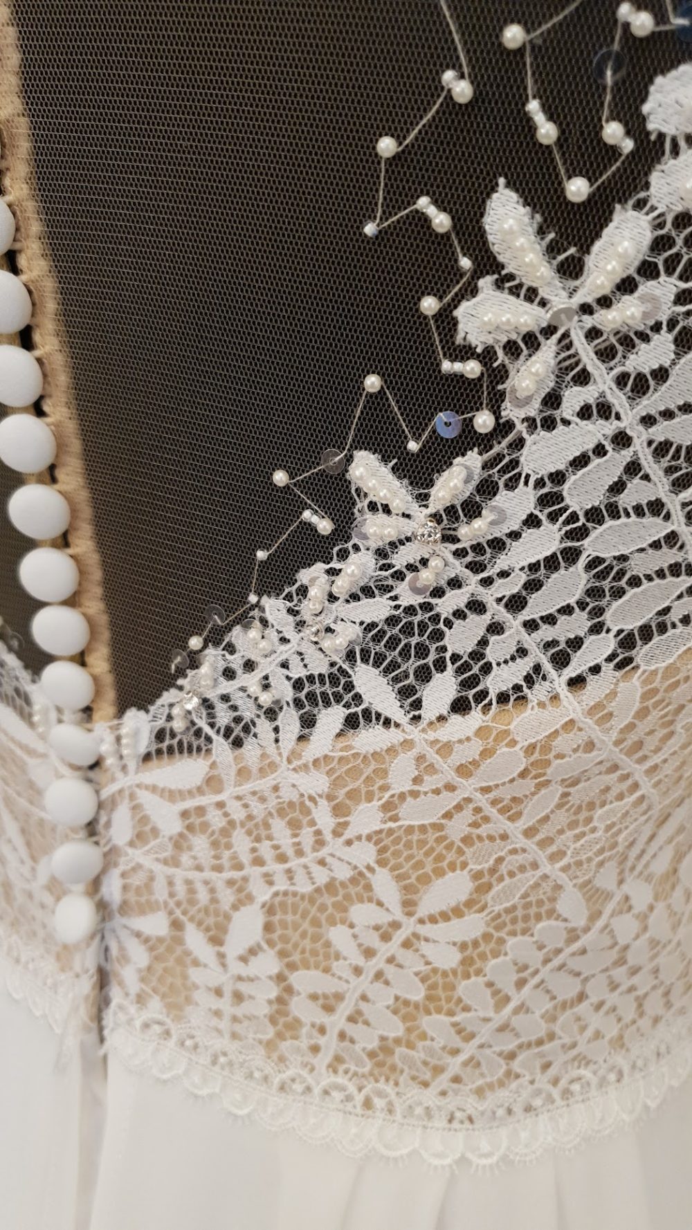 Lillian West. Model 66135. Super smuk pre-loved brudekjole med et let skørt i chiffon og en yderst dekorativ overkrop med nude bund og ivory blonde der er pyntet med perler. Kjolen har v-udskæring foran, lukket ryg og lange ærmer.