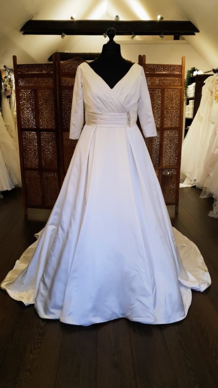 Smuk klassisk A-line brudekjole i en blød satin. Kjolen har draperinger på overkroppen og omkring taljen. V-udskæring både foran og bagpå. 3/4 lange ærmer og læg i skørtet med det lange slæb.