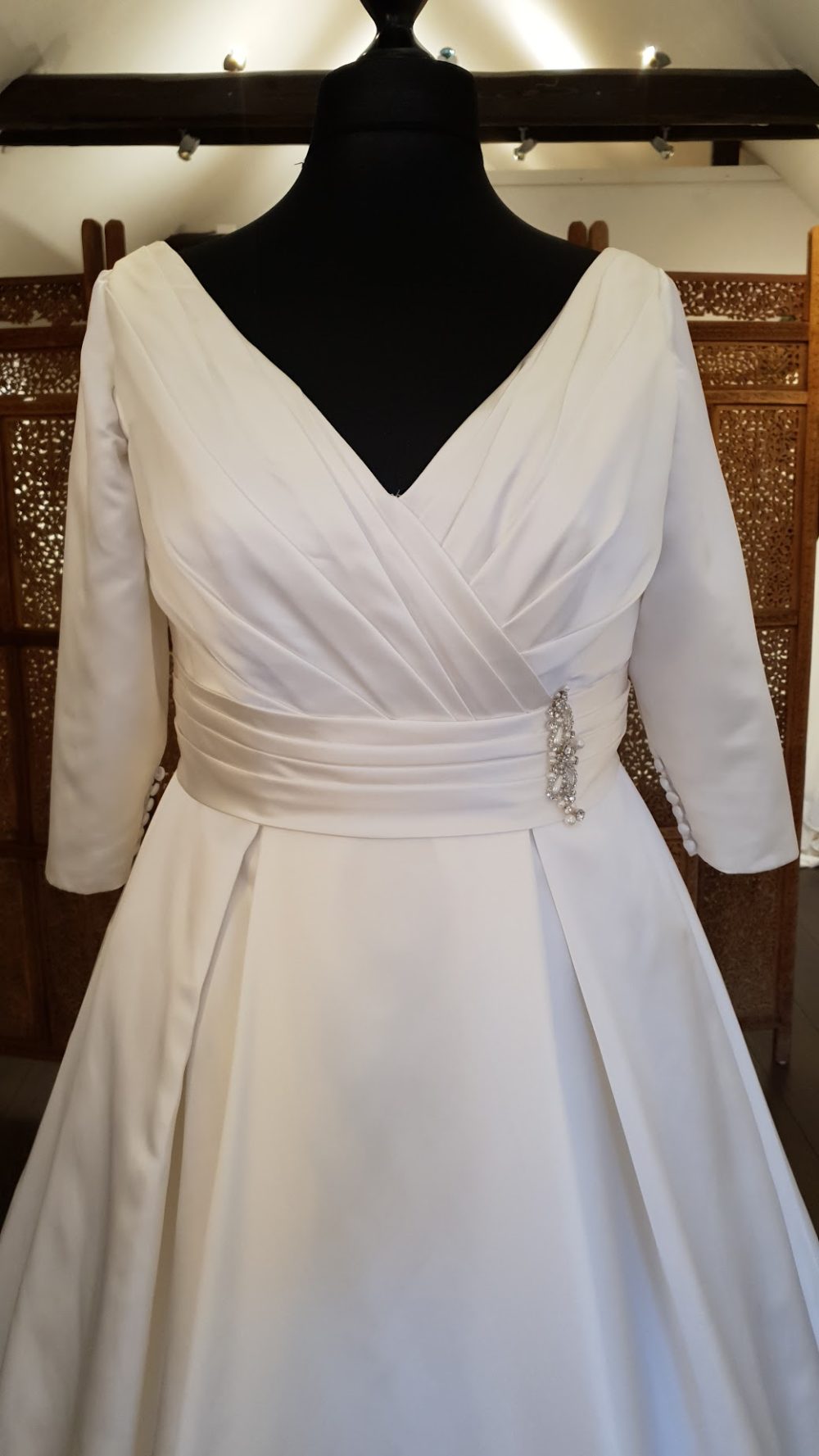 Smuk klassisk A-line brudekjole i en blød satin. Kjolen har draperinger på overkroppen og omkring taljen. V-udskæring både foran og bagpå. 3/4 lange ærmer og læg i skørtet med det lange slæb.