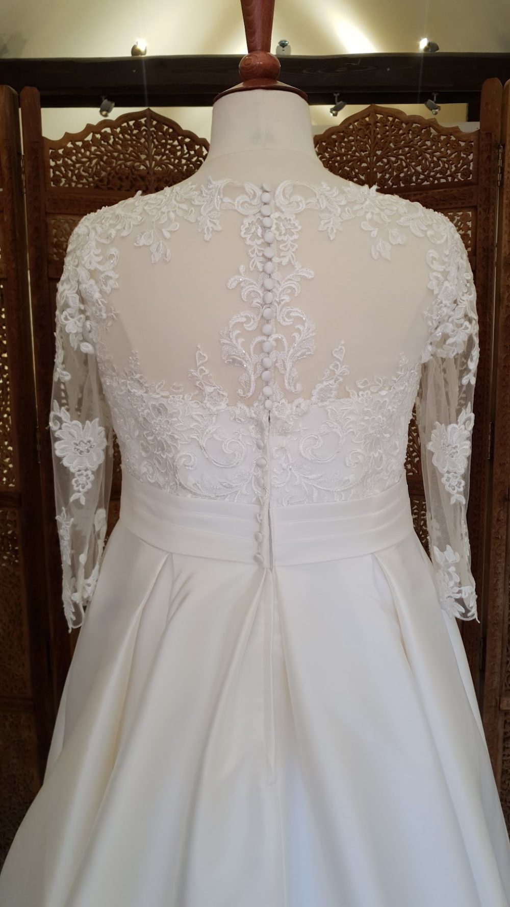 Klassisk og smuk A-line brudekjole med blonder på overkroppen og et skørt i satin. Kjolen har 3/4 lange blondeærmer og en lukket ryg med stofbetrukne knapper.