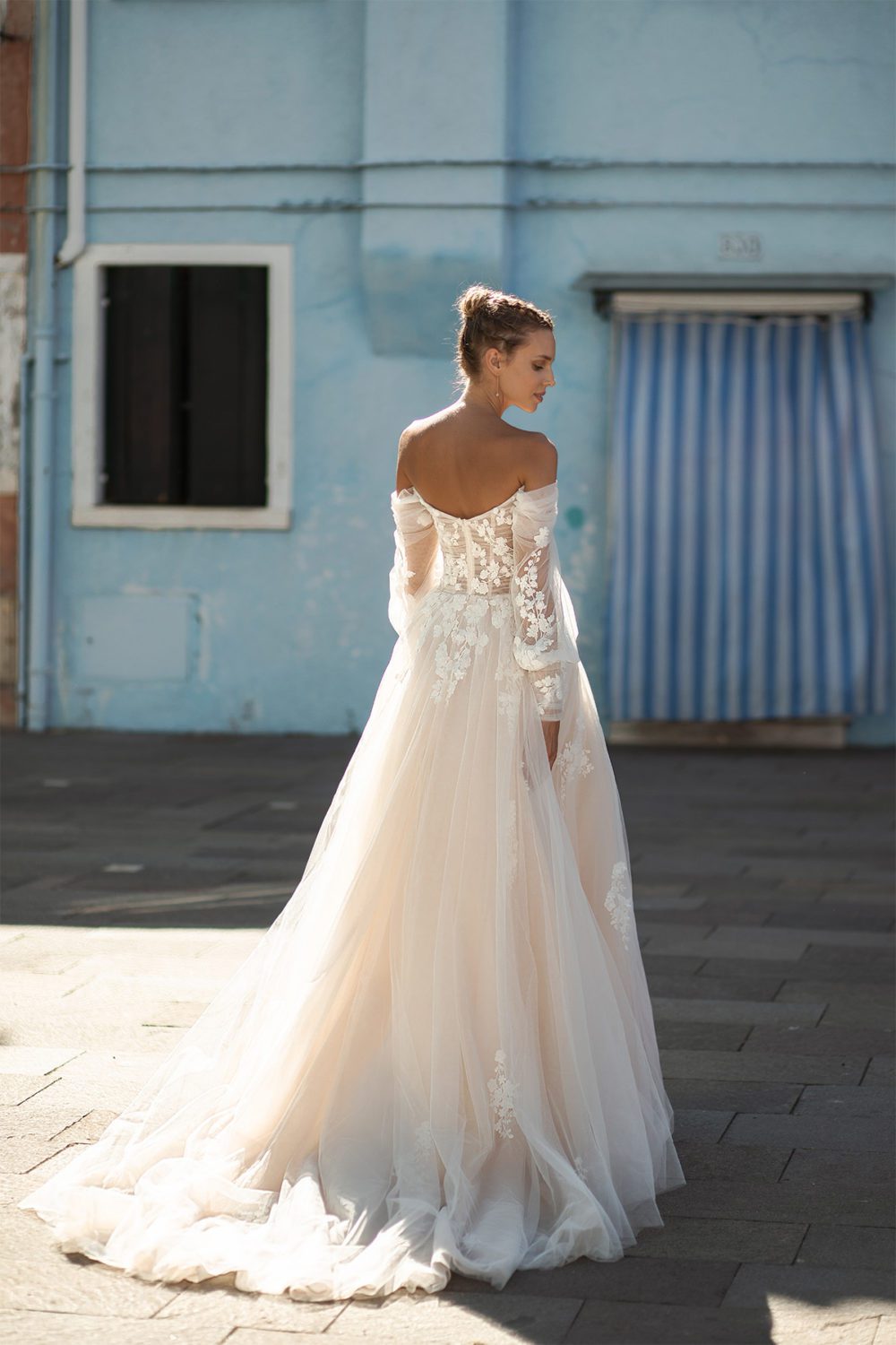 Maria Anette. Model 5410. Smuk A-line brudekjole i tyl med bådudkskæring og lange off-shoulder ærmer. Kjolen har en smuk ferskenfarvet nuance.