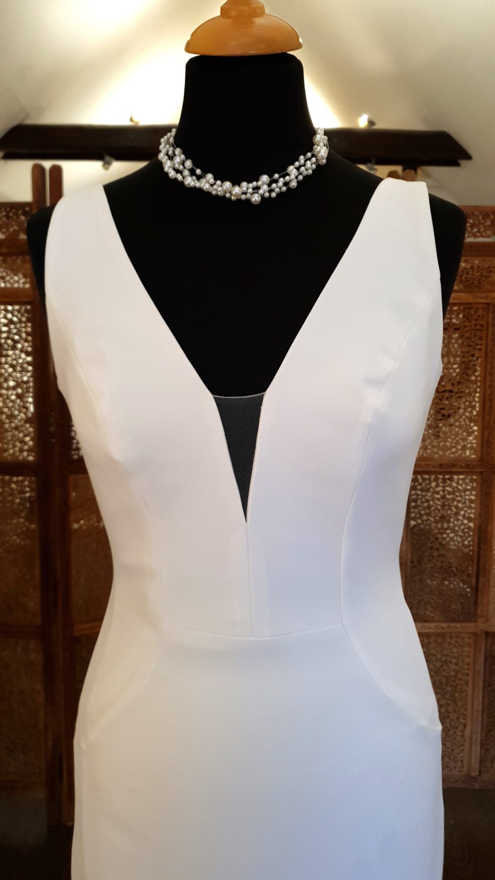 Pronovias. Elegant smuk og minimalistisk slank brudekjole i crepe. Kjolen har v-udskæring brede stropper og dyb v-udskæring på ryggen. Der er stofbetrukne knapper hele vejen ned af ryggen og ud på det lange slæb.