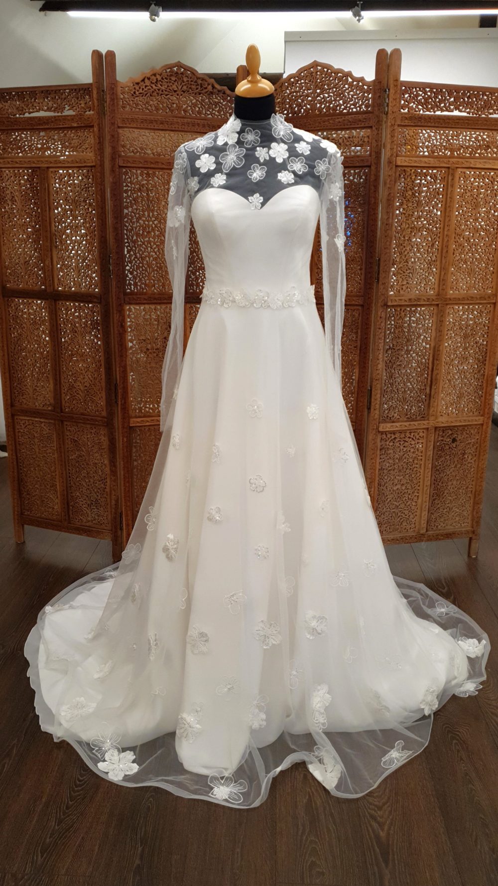 A-line brudekjole bestående af model Harmonia corsagekjole i chiffon fra Bianco Evento og en langærmet kappe i mesh med 3-d blomsterapplikationer. Dertil et blomsterbælte.