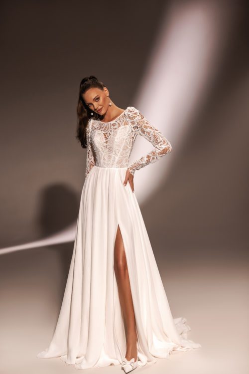 Katy Corso. Model Alen. Model Alen er en dejlig let A-line brudekjole med et skørt i chiffon. Skørtet har høj slids og et langt slæb. Øverste del af kjolen består af et corset med hjerteudskæring, som er dækket af en grov stormønstret blonde. Kjolen har lange ærmer med læg ved skuldrene og en lukket ryg.