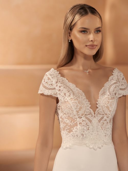 Bianco Evento. Bolero. Model E-426. Blondebolero med korte ærmer, v-udskæring både foran og bagpå, samt knapper i ryggen.