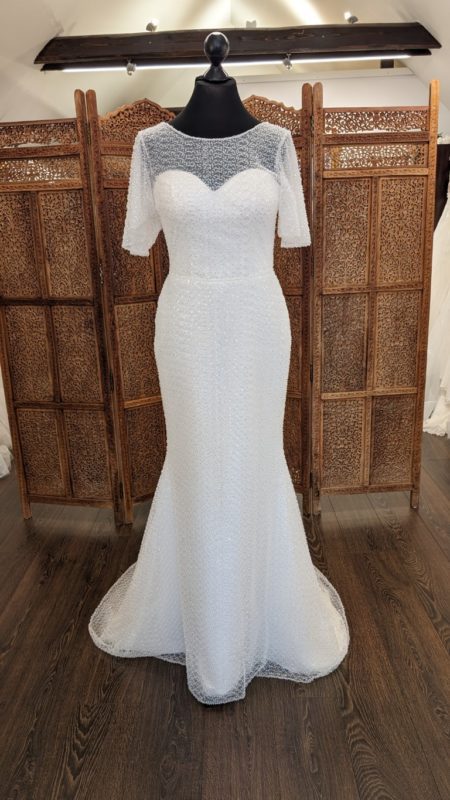 The Wedding Dress. Model Pealdream. Slank og elegant brudekjole med perler og pailletter fra top til tå. Kjolen Har høj rund halsudskæring med en hjerteudskåret corsage og v-udskæring på ryggen. Den har korte flagermus ærmer og et kort slæb.
