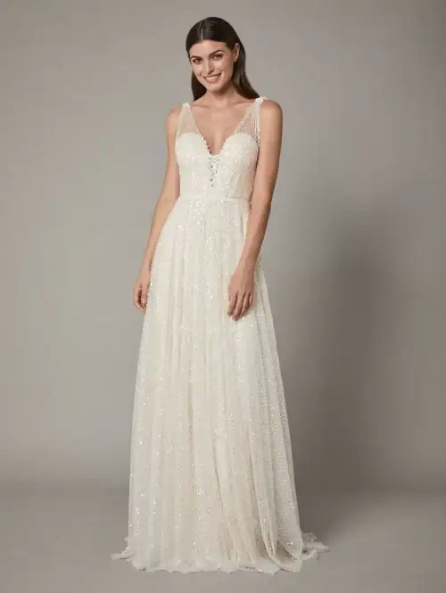 Ny og virkelig smuk A-line brudekjole med små fine detaljer. Kjolen har et indre lag med de smukkeste blonder og små 3-D blomser. Yderst har kjolen et ternet tyllag med blanke pailletter. Det yderste ternede tyl går op og danner stropper på en hjerteudskåret corsgar og de små 3-D blomster fortsætter med at give de smukkeste detaljer på kjolen. Sample sale.