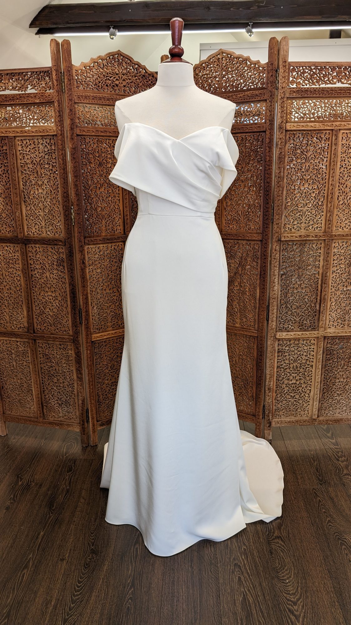 Jarice Bridal. Model ND22DE01. Smuk og elegant slank brudekjole i crepe. Kjolen har en form for slå-om effekt på overkroppen, der danner off-shoulder ærmer.