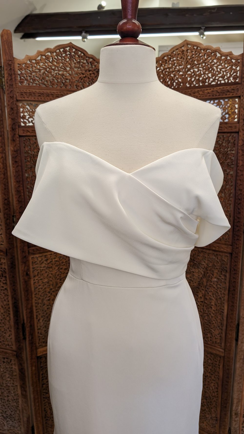 Jarice Bridal. Model ND22DE01. Smuk og elegant slank brudekjole i crepe. Kjolen har en form for slå-om effekt på overkroppen, der danner off-shoulder ærmer.