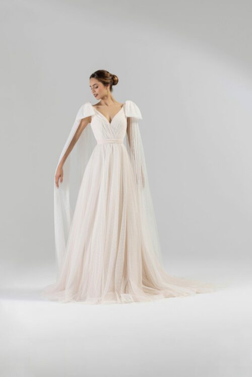 Eglantine Creations. Model Lovely. Smuk og feminin A-line brudekjole i prikket tyl. Kjolen har v-udskæring både foran og bagpå. På skuldrene er den forsynes med store sløjfer der falder ned over armene og danne en form for kappe.