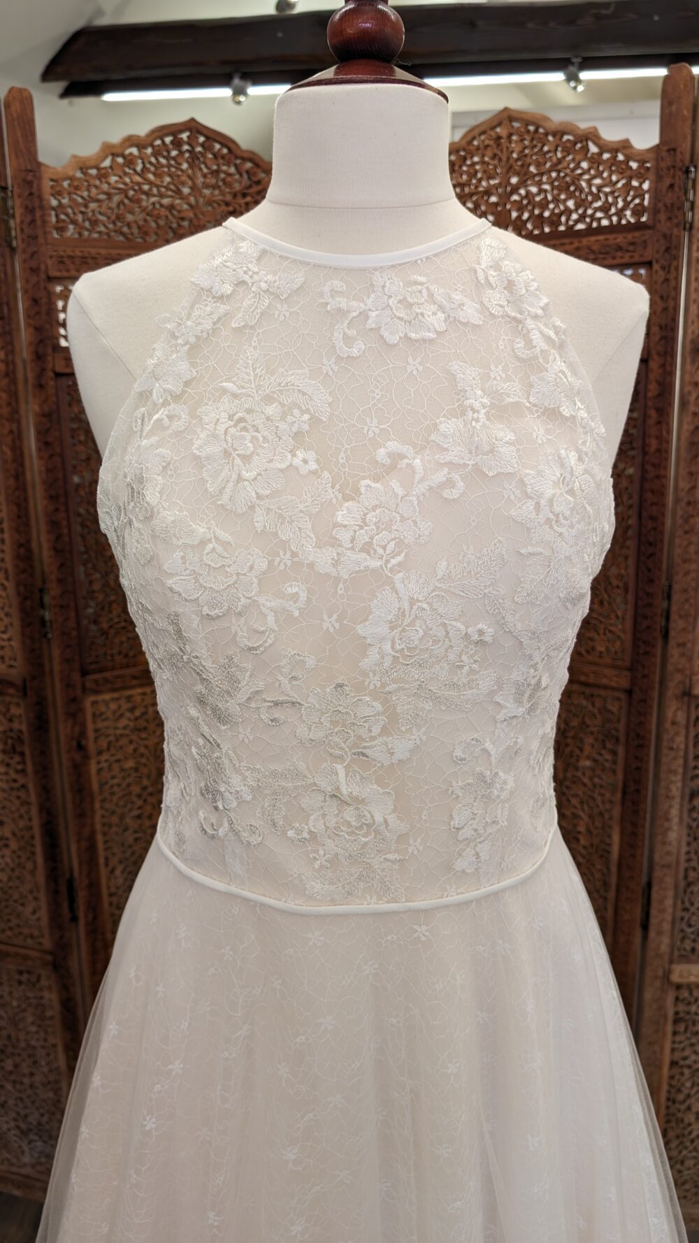 The weddingdress by Marielou. A-line brudekjole i sarte blonde med nude bund. Kjolen har høj halsudskæring både foran og bagpå.