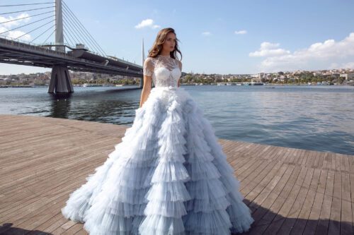 Maria Anette. Model 5237. Stor fyldig prinsessekjole i tyl med flæser i hele skørtet. Kjolen har en dekoreret overkrop i mesh, men perlebroderi og korte ærmer. Den har høj rund halsudskæring og lukket ryg.