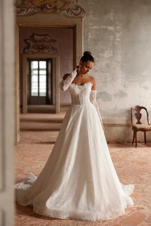 Ivory Bridal Fashion. MOdel Verona. Smuk og romantisk A-line brudekjole med blonder fra top til tå. Kjolens hjerteudskårne corsage er i kanten dekoreret med 3-D blomster, som også ses i toppen på de aftagelige lange ærmer. Kjolen har en dekorativ snøre i ryggen og en smukt langt slæb.