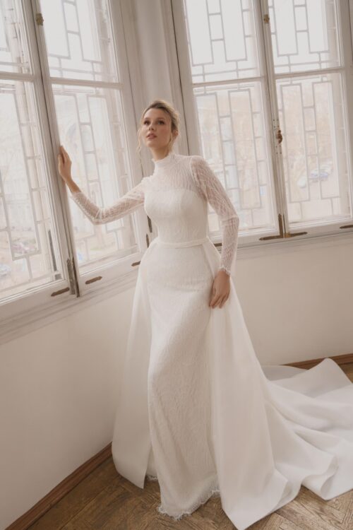 Ivory Bridal Fashion. Model Lancome. Smuk og elegant slank helblondekjole med aftageligt slæb. Kjolen har lange ærmer og høj hals med krave. Den er en anelse transparent i overkroppen, så den hjerteudskårede corsage ses igennem de smukke blonder.