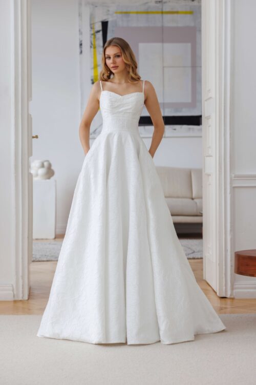 Jarice. Model Aluna. A-line brudekjole i en blomstervævet satin. Kjolen har lidt draperinger på overkroppen, spagettistropper, lommer i skørtet og slæb.