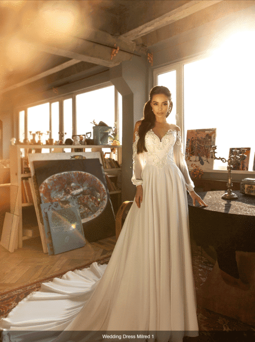 Jasmin Empire. Model Milred. Smuk A-line brudekjole i chiffon, med lange bollonærmer. Kjolen har illusionen af bådudskæring, med nude mesh op til en rund halsudskæring. Overkroppen har dekorative blondeapplikationer og kjolen har et langt slæb.