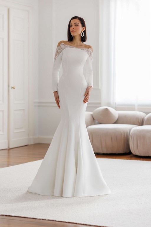 Jarice Bridal. Model Art 26-10. Smuk minimalistisk havfruekjole i Mikado satin med lange ærmer. Kjolen har en blondedetalje som danner bådudskæring, går ned i en spids på armene og danner en smuk lukket og transparent v-udskæring på ryggen.