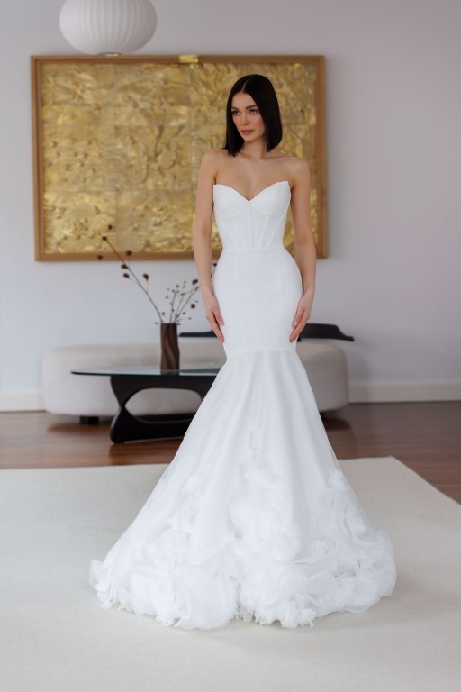 Jarice Bridal. Model Beloved. Smuk og minimalistisk havfruekjole med de vildeste 3-D blomster på skørtet og slæbet. Kjolen er i en elastisk crepe i overkroppen og skørtet i tyl. Den har kat-eye udskæring og stivere der danne slankene linjer i overkroppen og får den til at sidde helt perfekt.