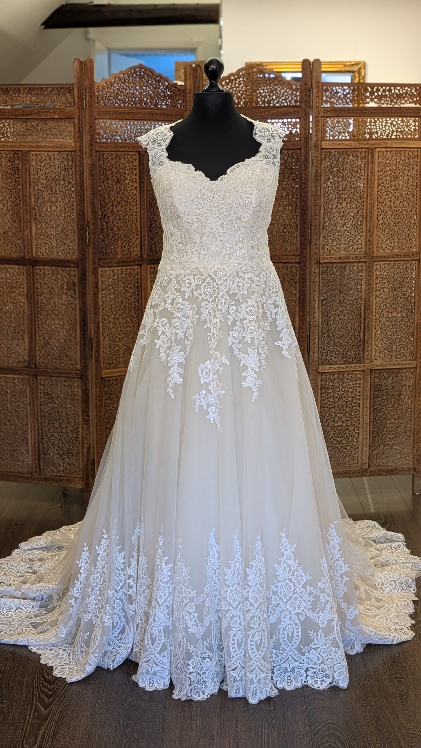 Morilee by Madeline Gardner. Model Julietta. Smuk og romantisk A-line brudekjole med dekorative blonder. Kjolen er champagnefarvet har Queen Anne udskæring og en helt lukket transparent blonderyg.. Den har stofbetrukne knapper i lukningen og et meget smukt slæb.