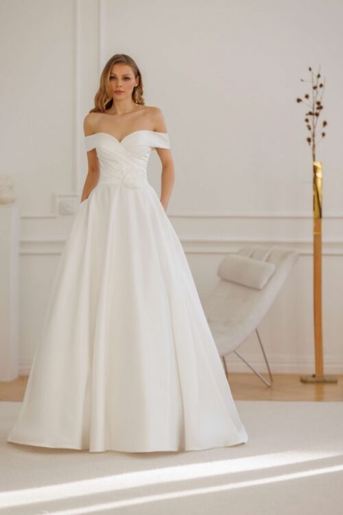 Jarice Bridal. Model Salou. Smuk og enkel A-line brudekjole i Mikado satin med draperinger på overkroppen, off-shoulder stropper og blomsterdetaljer i den ene side af taljen. Kjolen har desuden lommer og et lang slæb.