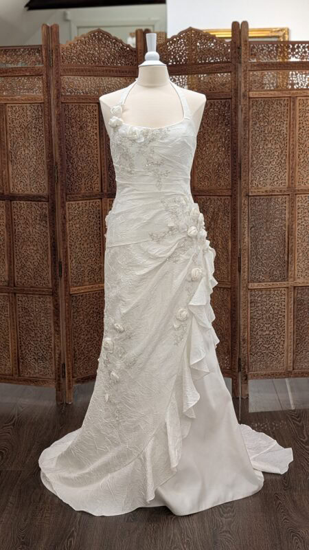 Couture Lotus Paris. Romantisk slank brudekjole i "krøllet" satin med smukke detaljerede broderier og 3-D blomster. Kjolen har halterneck og et asymmetrisk skørt med flæser.