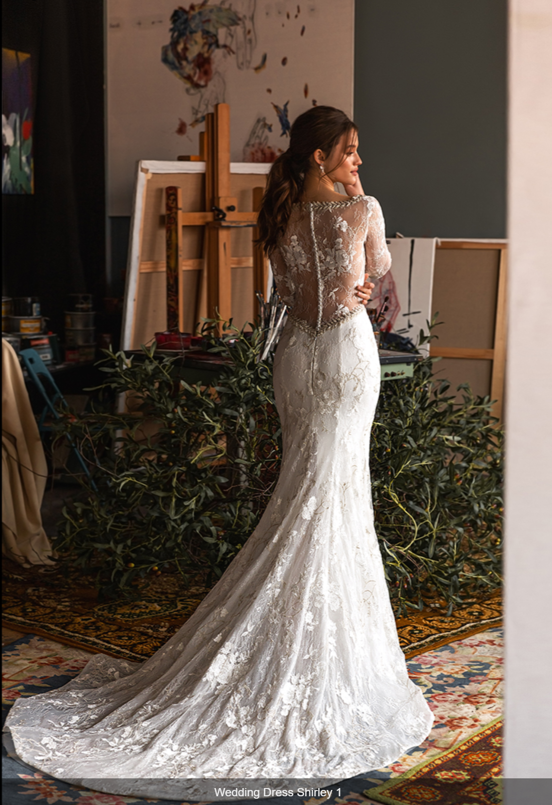 Jasmin Empire. Model Shirley. En smuk og dekorativ slank og langærmet brudekjole med kobbertråd og broderinger. Kjolen har illusionen af dyb kavalergang, men har høj bådudskæring . Ryggen er lukket men helt transparent og giver illusionen af dyb udskæring.