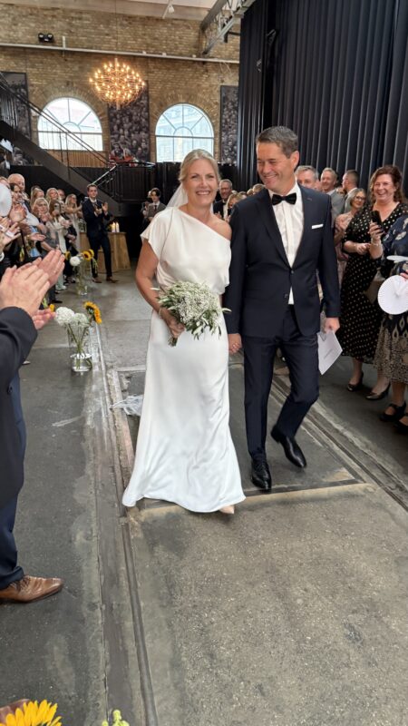 Rikke Gudnitz. Smuk elegant og minimalistisk brudekjole i en lækker satin. Kjolen er slank men stadig A-line. Den er løs i overkroppen og har et asymmetrisk cut med en båduskæring der gør at den ene skulder ere fri. Skøret har et megeet lille slæb.