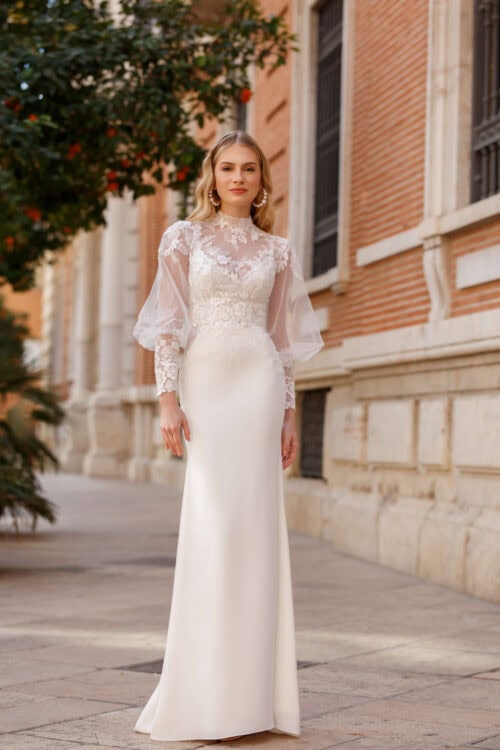 Jarice Bridal. Model Reggie. Smuk slank brudekjole med tilhørende blondebolero. Kjolen har spagettistropper og v-udskæring både foran og bagpå. Blondeoverdelen har højhals og ballonærmer i mesh, som bliver til blonde og slanke ærmer i hele underarmen.