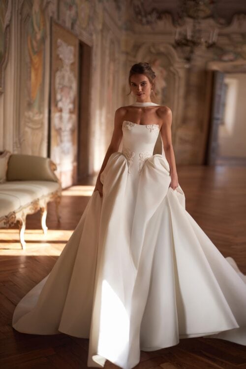 Ivory. Model Amalfi. Sofistikeret og iøjnefaldende brudekjole. Den er både klassisk og moderne med sit dramatiske look. Kjolen er i satin. har en slank silhuet fra corsage og hele vejen ned i midten af skørtet. Resten af skørtet er volumiøst. Corsagen er i udskæringen samt ved taljen pyntet med et smukt perlebroderi.