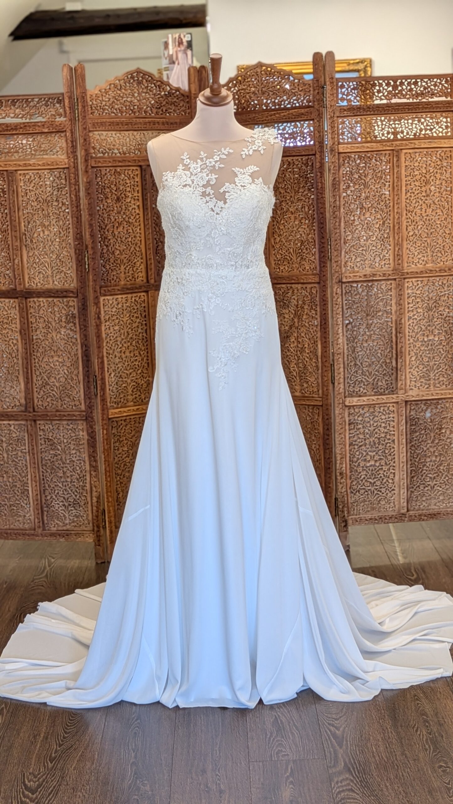 White One. Model Figura. Meget smuk A-line brudekjole med chiffonskørt. Kjolen har en hjerteudskåret corsage, som er dækket af blonder der på den dekorativ og elegant måde brede sig op mod halsen og asymmetrisk over den ene skulder for så at forsætte ned på en dyb udskåret ryg. Kjolen har sidelynlås.