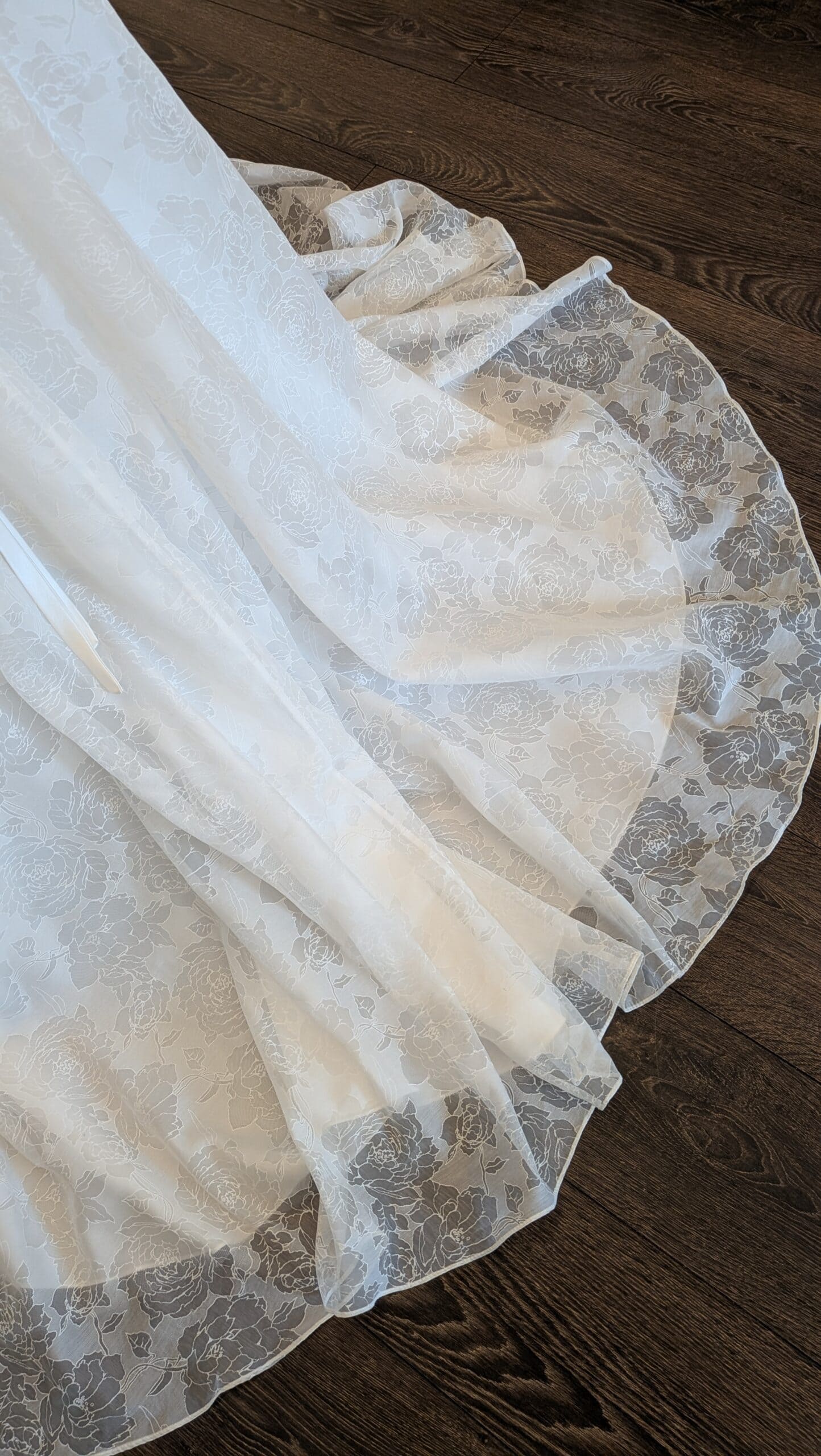 Callista. Pre-loved brudekjole i jaquard stof. Kjolen har en drapperet overkrop, brede stropper og v-udskæring både foran og bagpå. Taljeskærringen sidder lavt og der er snøre i ryggen, som gør kjolen mere fleksibel i størrelsen. Det lille element af rhinsten i taljen kan nemt fjernes. Slæbet er ikke så langt.