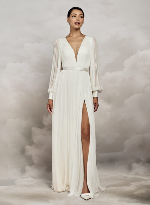 Catherine Deane. Model Levi. Let og elegant langærmet A-line brudekjole i 100 % silketyl. Kjolen har dyb v-udkskæring både foran og bagpå. Ballonærmerne er transparente og afslutes med en smuk bred manchet der lukkes med stofbetrukne ærmer. Kjolen har et påsyet glat bånd i taljen, høj slids i skørtet og et lille slæb.