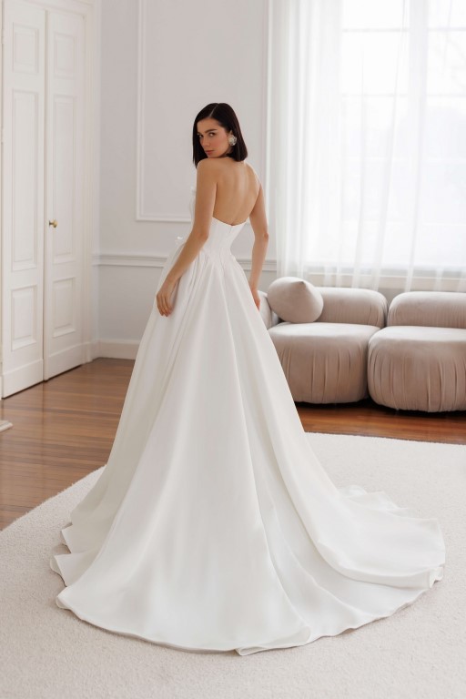 Jarice Bridal. Model Art 26/23. Smuk enkel og stropløs prinsessekjole i satin. Kjolens corsage er hjertudskåret, har synlige stivere og en dyb kavalergang. Den er yderligere forsynes med skåle der titter op over udskæringen der er pyntet med 3-D blomstter og perler. Pynten fortsætter ned af kavalergangen og sidder også rundt i hele taljeskæringen. Skørtet har store læg og slæb.