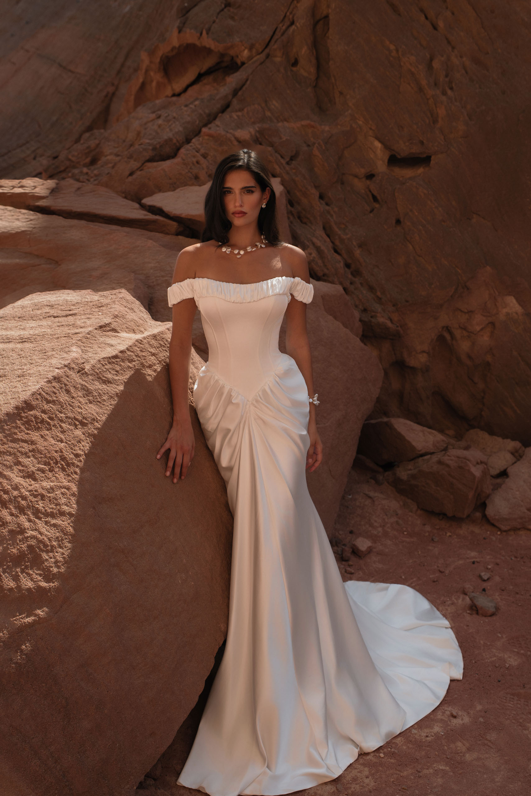Katy Corso. Model Asha. Smuk slank satinkjole med draperinger som fremhæver de kvindelige former. Kjolen har drop waist line, stivere i corsagen og off-shoulder stropper.