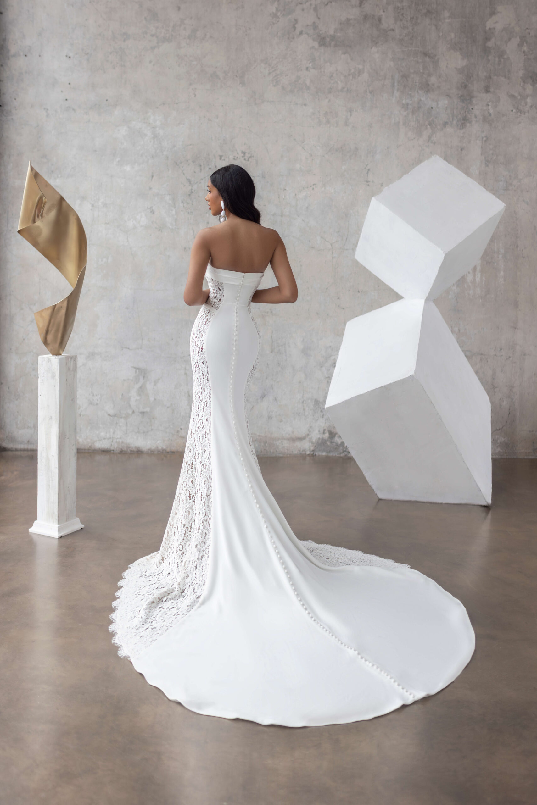 Jarice Bridal. Model Fabienne. Smuk og elegant slank brudekjole. Kjolen er stropløs, har lige skærring over barmen og har detaljer som lette draperinger over barmen, lodrettet stivere i overkroppen og blonder der er dekorert med perler og pailetter i taljen. Det unike ved denne kjole er helt klart de brede blondepartier, som følger fra overkroppen og hele vejen ud på slæbet og fremhæver figuren, på smukkeste vis.
