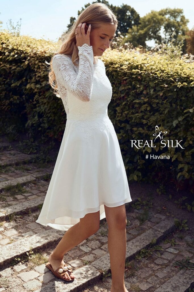 Real Silk Havana konfirmationskjole fra siden med blondeærmer, tætsiddende overdel og high-low-skørt