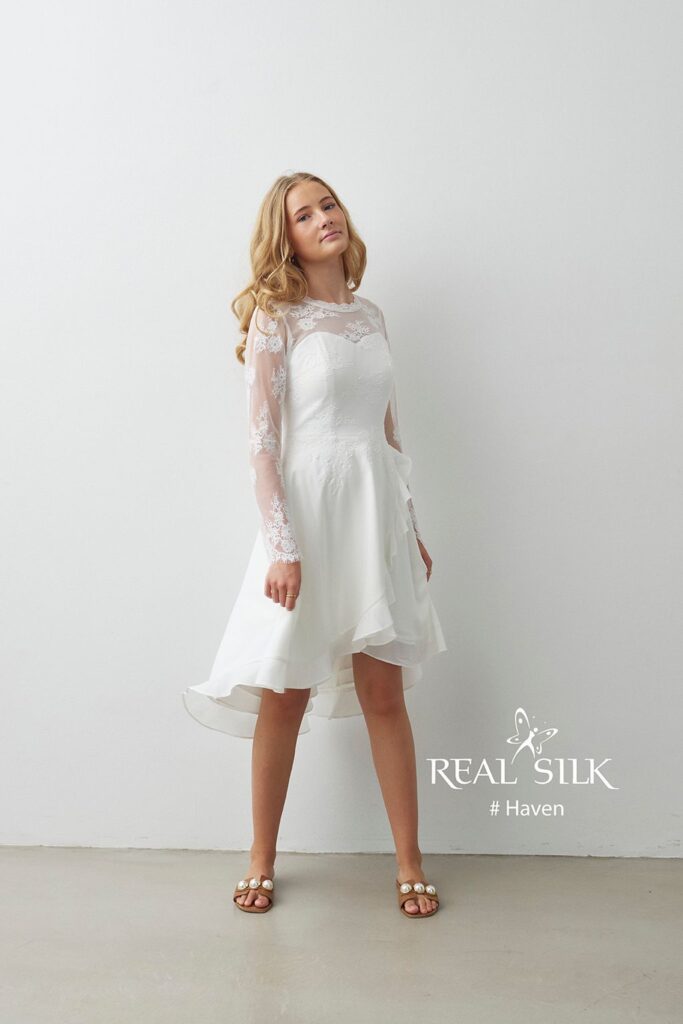 Real Silk Haven konfirmationskjole i bevægelse med transparente blondeærmer og asymmetrisk flæseskørt