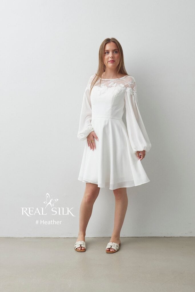 Real Silk Heather konfirmationskjole med transparent blomsterdetalje, lange ballonærmer og knælangt A-formet skørt