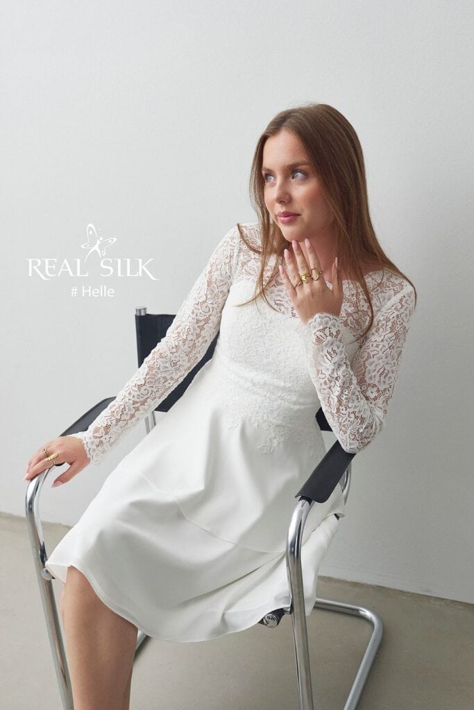 Frontdetalje af Real Silk Helle konfirmationskjole med blomsterblonde, lange ærmer og glat peplum
