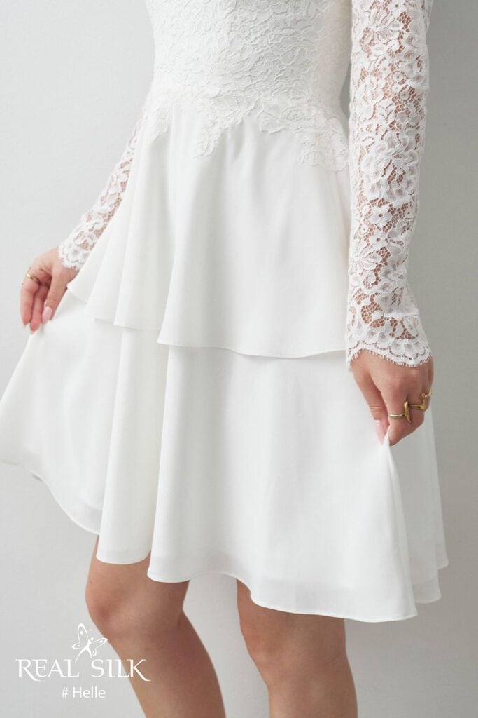 Skørtdetalje på Real Silk Helle konfirmationskjole med glat peplum, todelt fald og blondeærmer