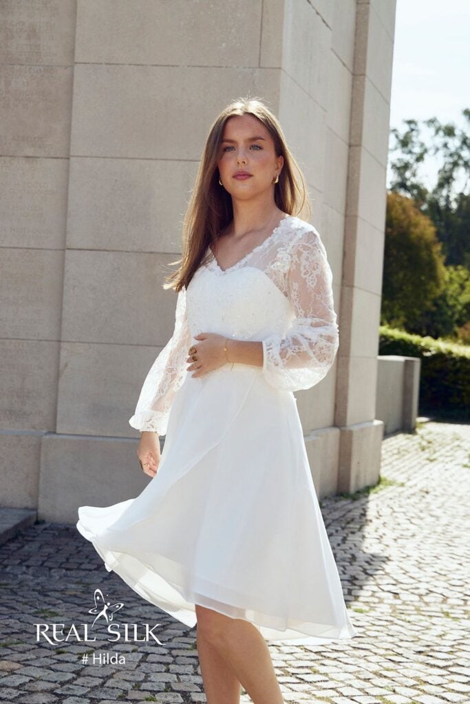 Real Silk Hilda konfirmationskjole med hjerteformet overdel, lange blondeærmer og high-low-skørt