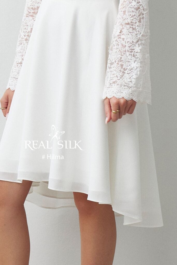 Skørt- og ærmedetalje på Real Silk Hilma konfirmationskjole med high-low-fald og lange blondeærmer