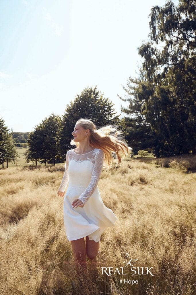 Real Silk Hope konfirmationskjole i bevægelse med transparente blondeærmer og let, knælangt skørt