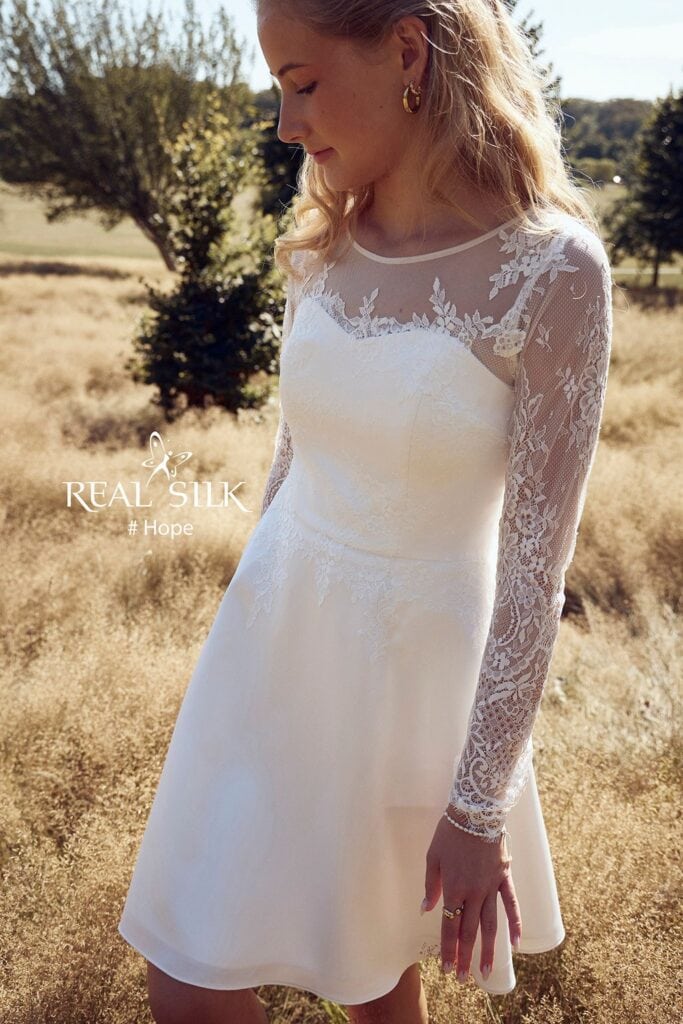 Frontdetalje af Real Silk Hope konfirmationskjole med transparent tyl, grenformet blonde og lange blondeærmer