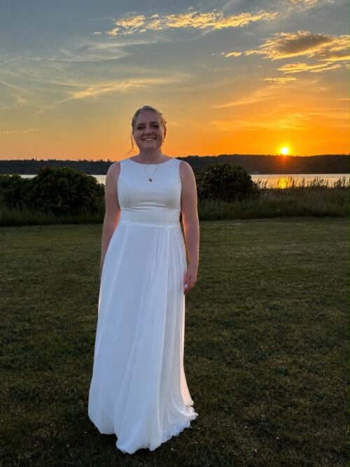Pre-loved A-line brudekjole i chiffon. Kjolen har høj bådudskæring og dyb ryg. Der er en meget enkel og påsyet blondebånd i taljen.